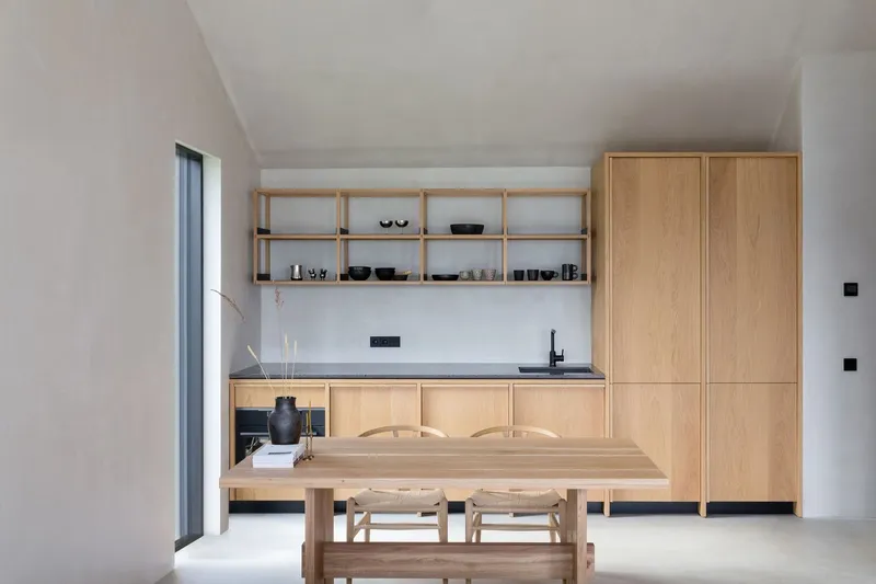 Oak kitchen with open shelving, tall cabinets, and a dining table under vaulted ceilings