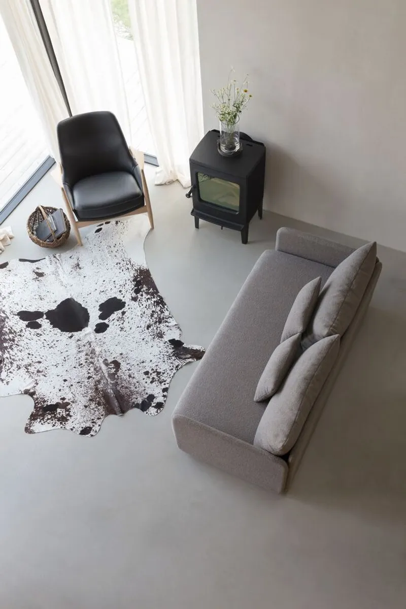 Top-down view of a living space with grey sofa, black armchair, wood stove and cowhide rug on polished concrete floor