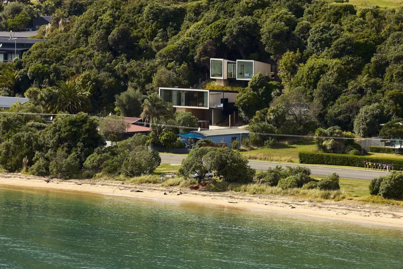 View from the water showing stacked volumes set into forested hillside above the shoreline