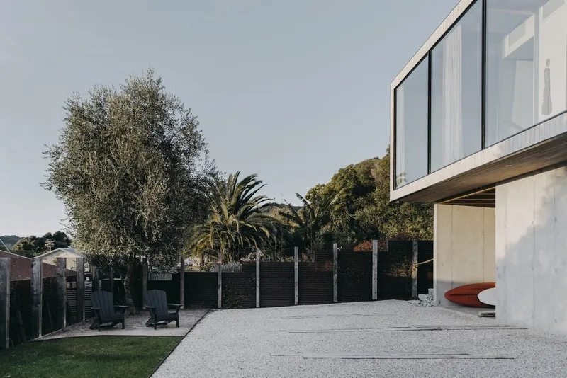 Gravel driveway and lawn beneath cantilevered upper volume clad in vertical timber and glass