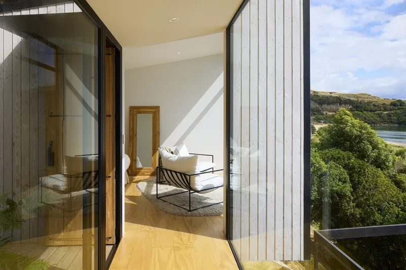 Upper level balcony with vertical metal cladding overlooking coastal bay and vegetated slopes