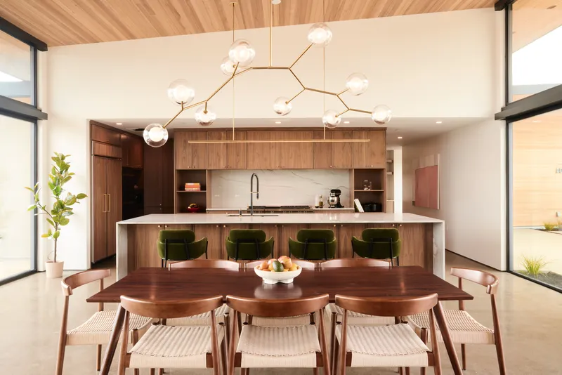 Open kitchen with walnut cabinetry and island featuring green velvet stools beneath a timber ceiling