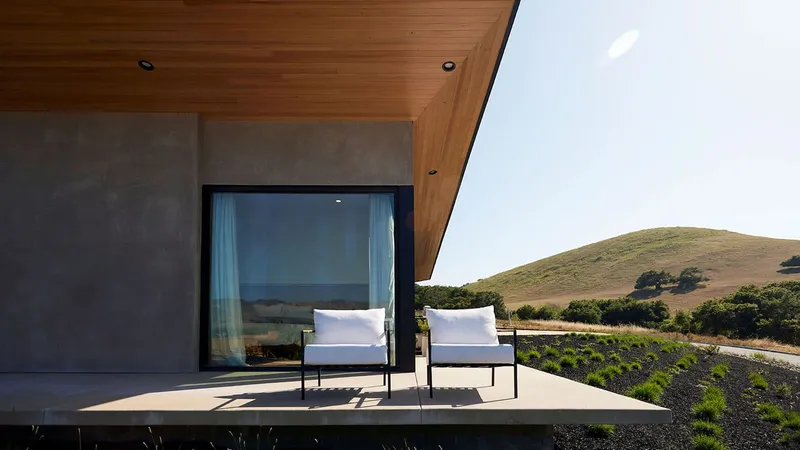 Covered terrace with timber soffit and two white chairs facing rolling hills in afternoon sun