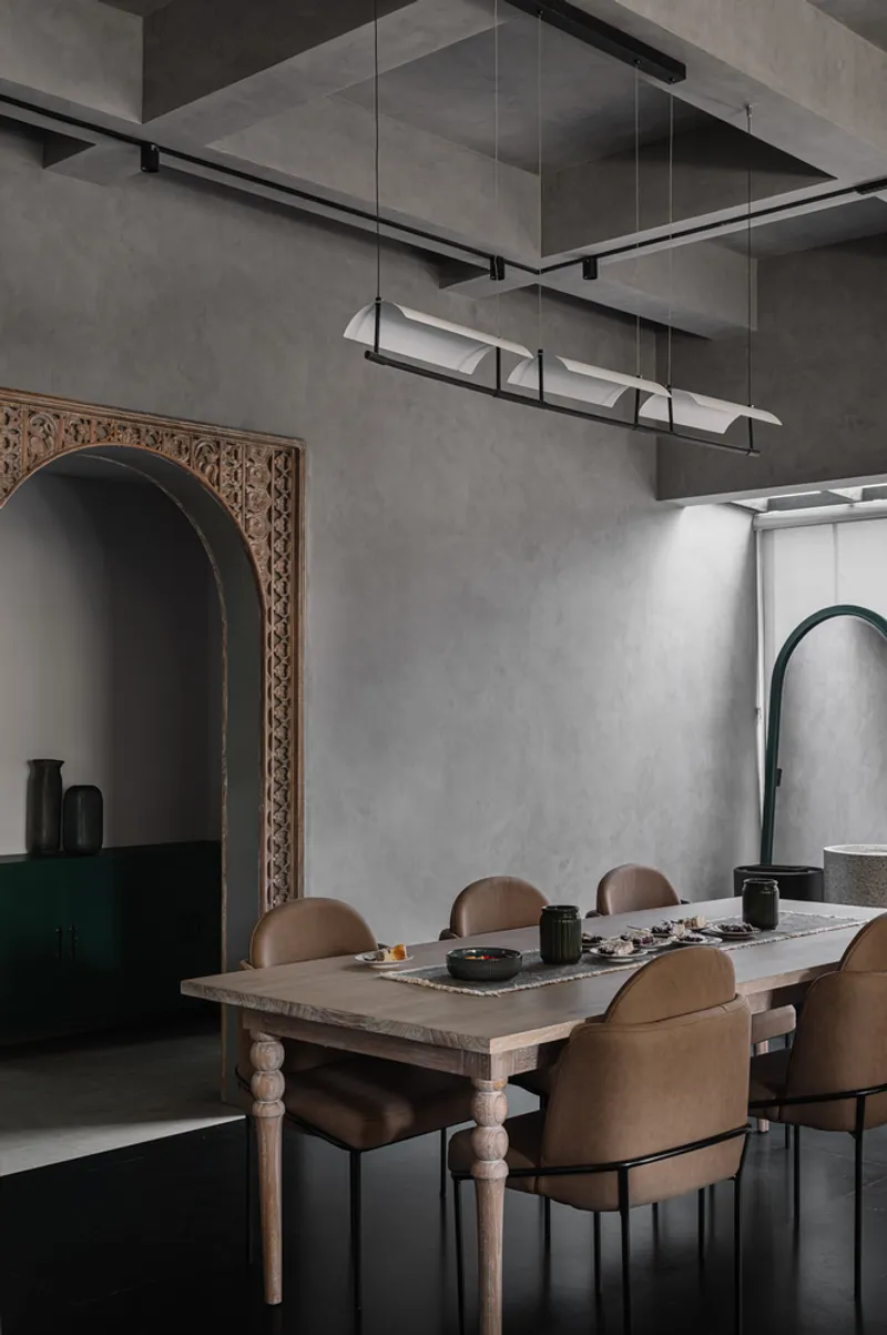 Dining table beneath a linear pendant light fixture with carved archway alcove to the left