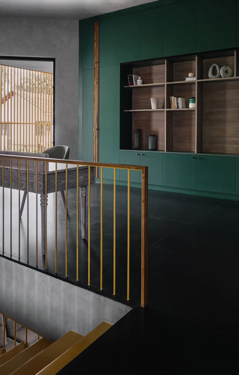 Upper landing with brass railing and green paneled cabinetry beyond a window overlooking the stair below