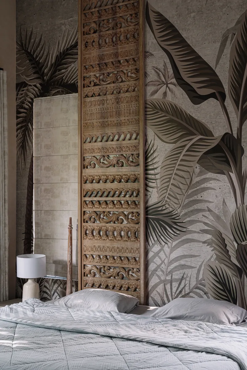 Bedroom with carved timber panel mounted above the bed against a wall mural of tropical palm leaves