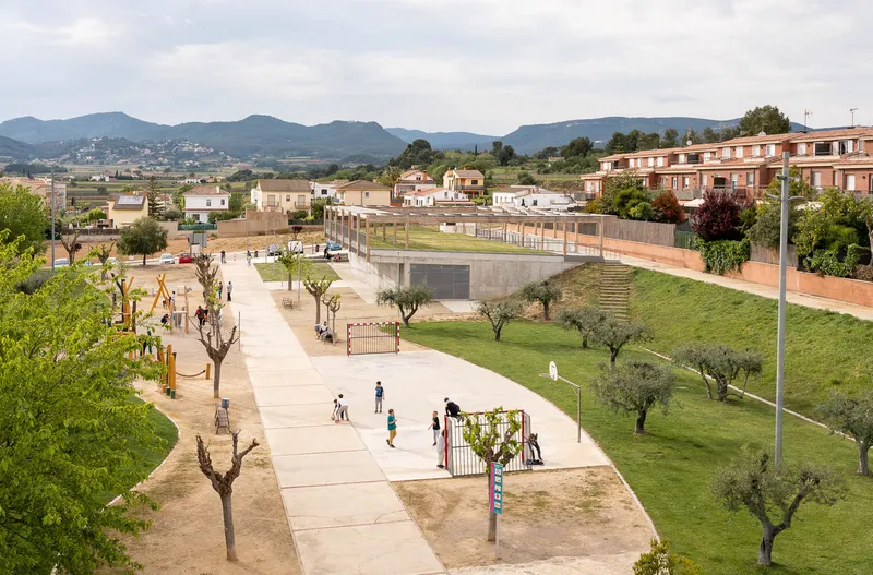 Elevated view of the public plaza with playgrounds, pruned trees and mountains visible in the distance
