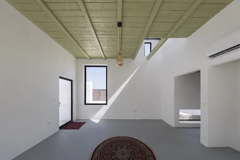 Interior room with green timber ceiling beams and white walls receiving sharp sunlight through black framed window