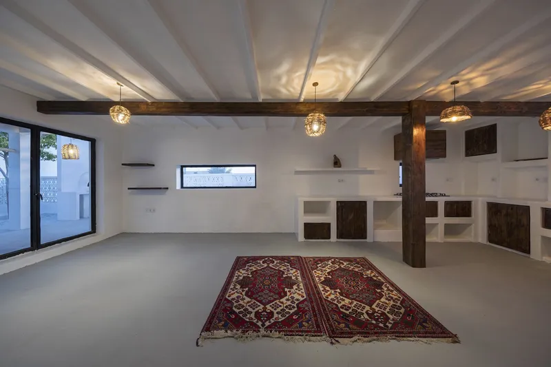 Kitchen space with white plaster counters, dark wood cabinetry, exposed timber columns and woven pendant lights overhead