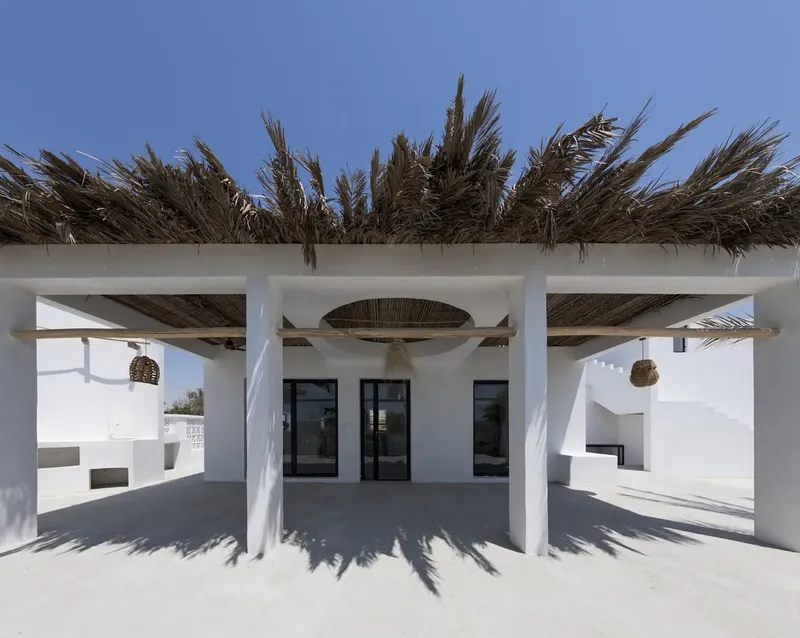Covered porch with arched reed canopy panel framing black window openings casting deep shadows on the floor