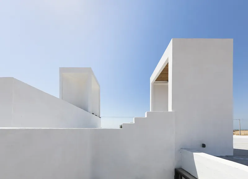 White rendered volumes with recessed openings and terraces under a clear blue sky