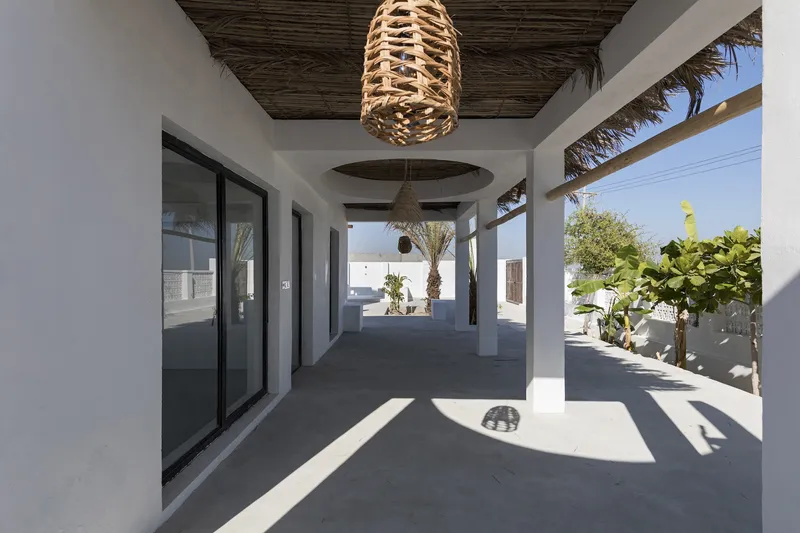 Covered terrace with woven pendant light and reed ceiling canopy framing views of palm trees and sky