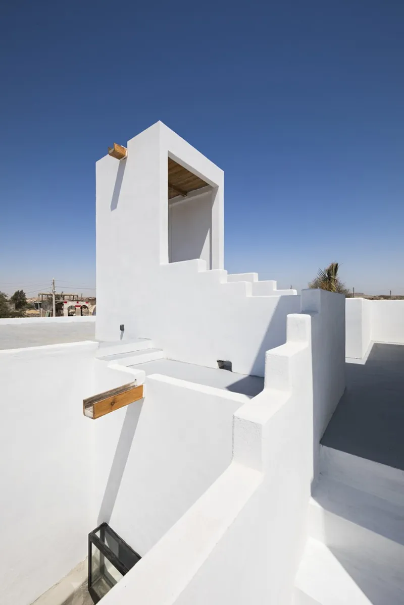 Rooftop terrace with white stucco tower accessed by exterior stairs and timber scupper in bright midday sun