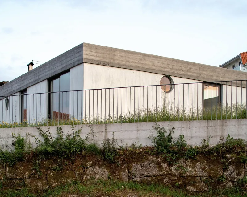 Horizontal wooden cladding facade with concrete retaining wall and circular window punctuating the pale timber slats