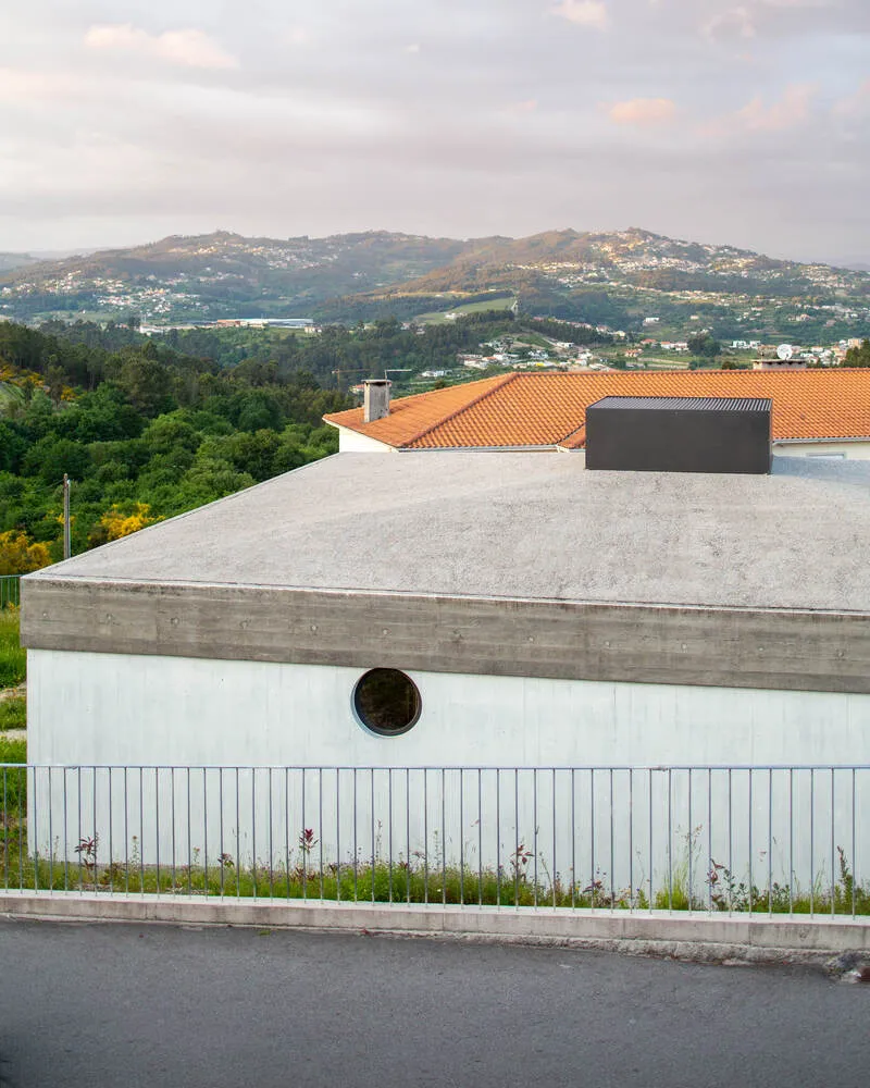 Street elevation showing vertical timber cladding with porthole window and concrete band beneath a flat roof with distant hills