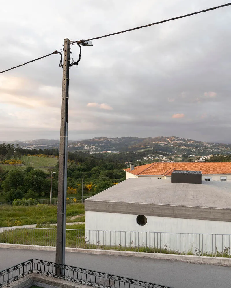 Concrete volume with circular vent and grey flat roof seen from a roadway under overcast skies