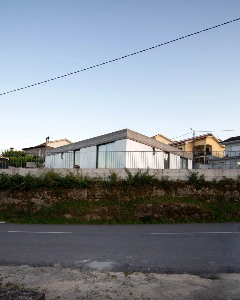 Street view of the corrugated metal facade and folded roof volume above an earthen embankment