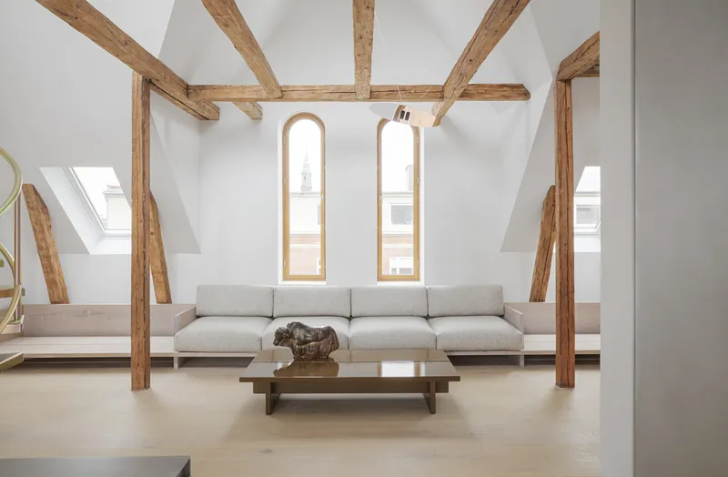 Attic living room with exposed timber beams and two arched windows framing the upholstered seating area