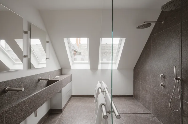 Attic bathroom with terrazzo vanity, glass-enclosed shower and skylight openings in sloped ceiling