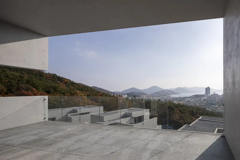 Rooftop terrace with glass railing overlooking coastal mountains and distant harbor
