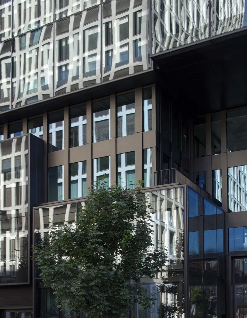 Street view of the mixed-material facade with a courtyard tree framed by glass and metal panels