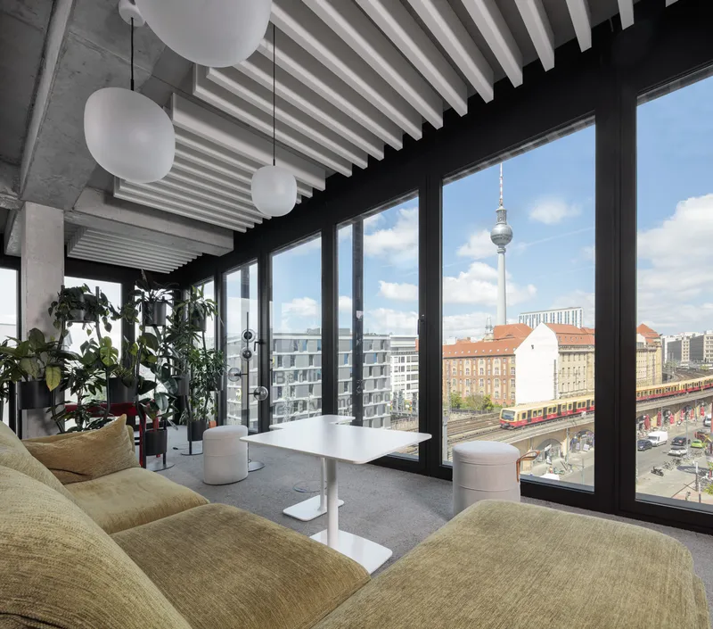 Interior lounge with exposed white ceiling beams and floor-to-ceiling windows overlooking the urban skyline