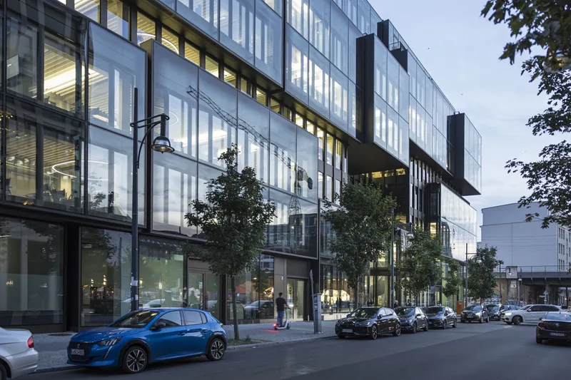 Translucent facade at dusk with interior lighting visible and street trees along the sidewalk