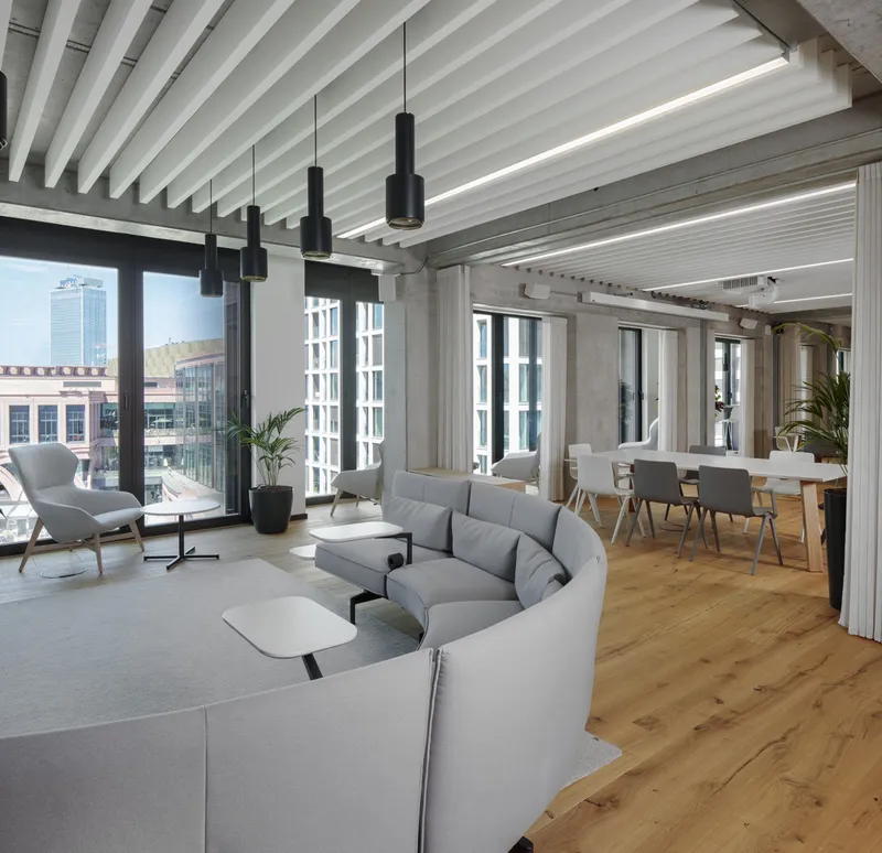 Open-plan interior with curved seating arrangement beneath white slatted ceiling and black pendant lights