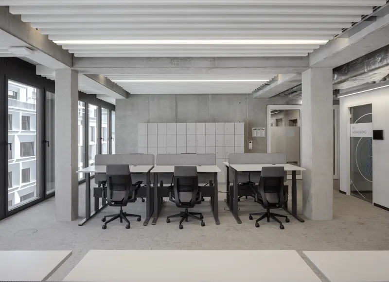 Open office space with exposed concrete ceiling beams, white baffle lighting and black-framed windows