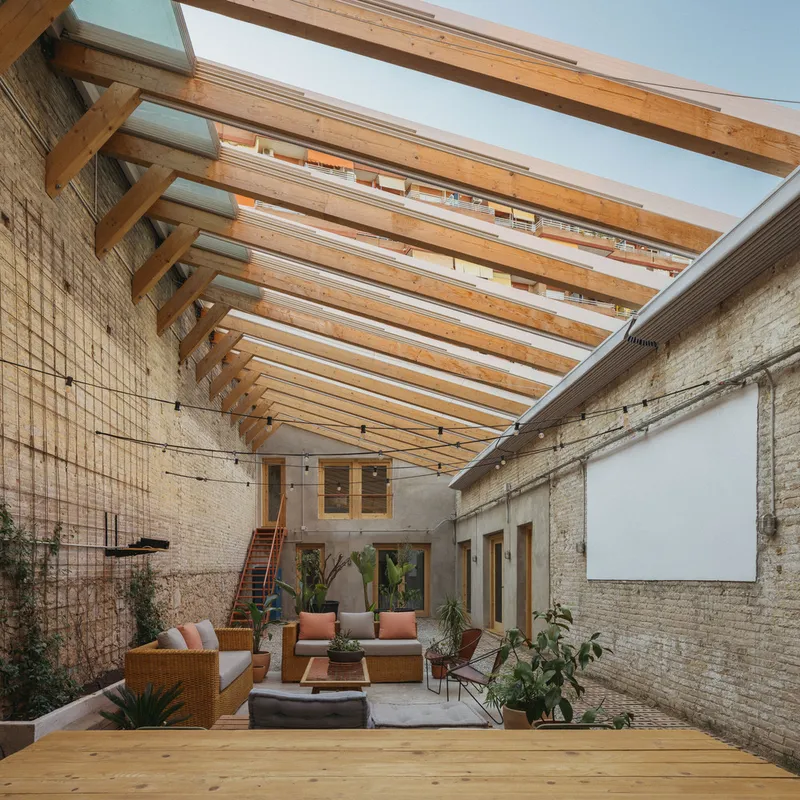 Interior courtyard with exposed timber roof beams, brick walls, and potted plants under open sky