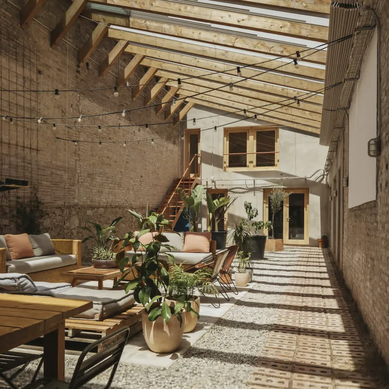 Courtyard with timber skylight, brick walls, potted plants, and afternoon sun casting shadows on patterned floor