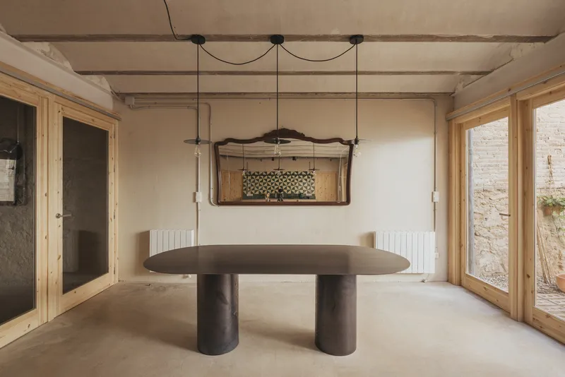 Interior room with cylindrical table on polished concrete, exposed timber beams overhead and pine-framed glazing
