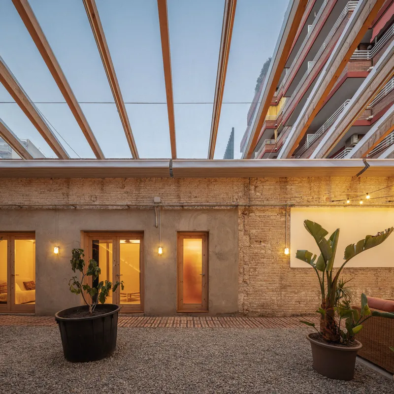 Courtyard at dusk with timber slat canopy overhead, exposed brick walls and potted banana plants
