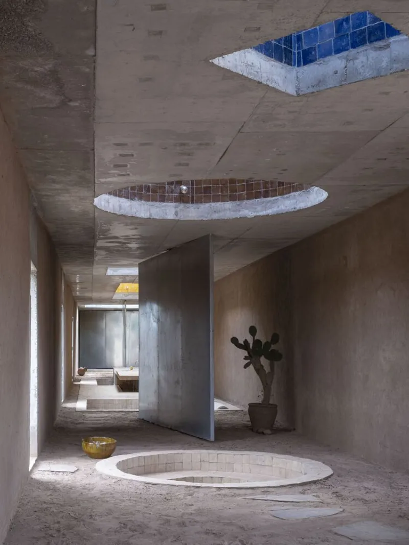 Interior corridor with board-formed concrete walls and ceiling cut by two tiled skylights above a floor pool