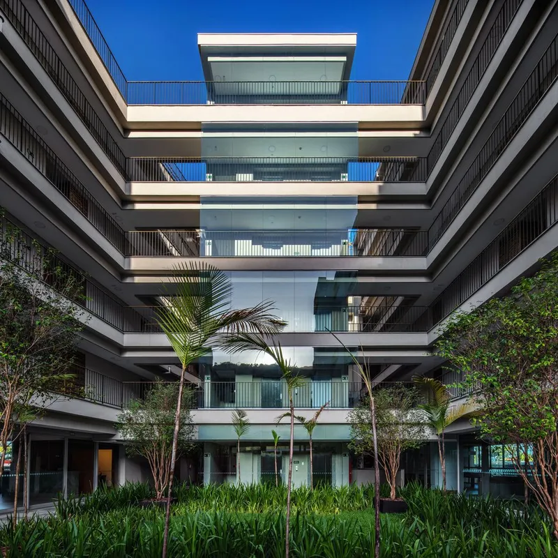 Courtyard view of stacked balconies framing a central glass core with planted palms and tropical vegetation below