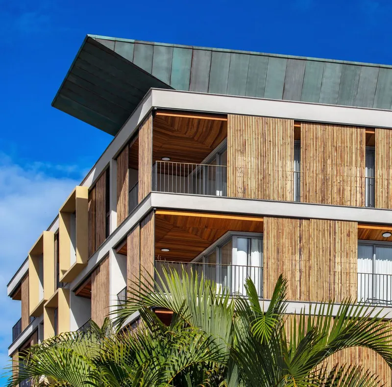 Corner facade detail showing vertical timber slats and wood soffit balconies with palms in the foreground