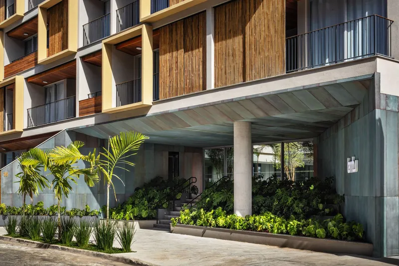 Ground level entrance with concrete canopy soffit sheltering planted beds and a bicycle near the lobby