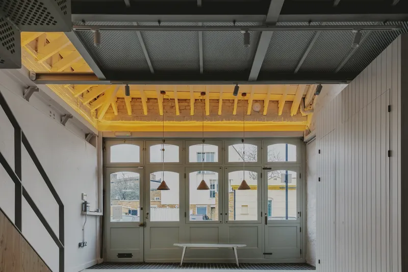 Entry hall with exposed yellow timber trusses above grey doors and hanging pendant lights