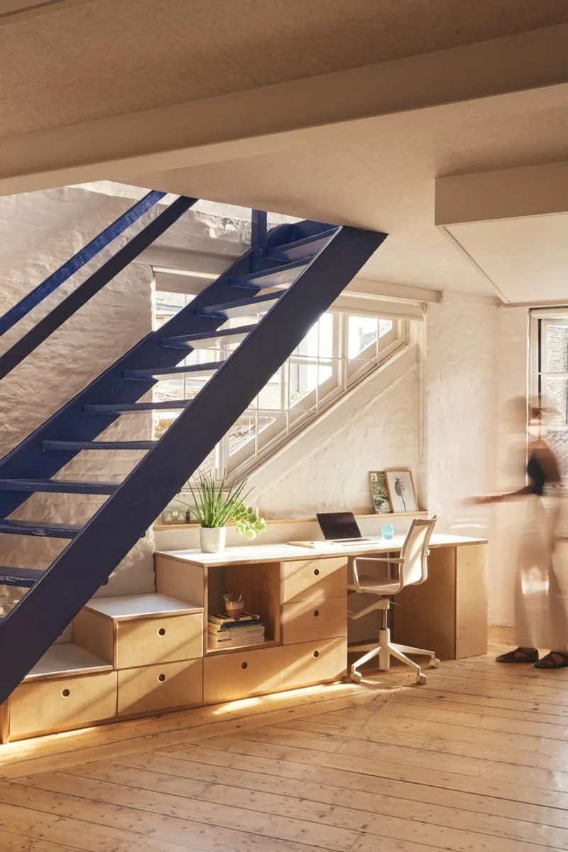 Blue open-riser staircase beside a timber desk with drawers and a blurred figure passing