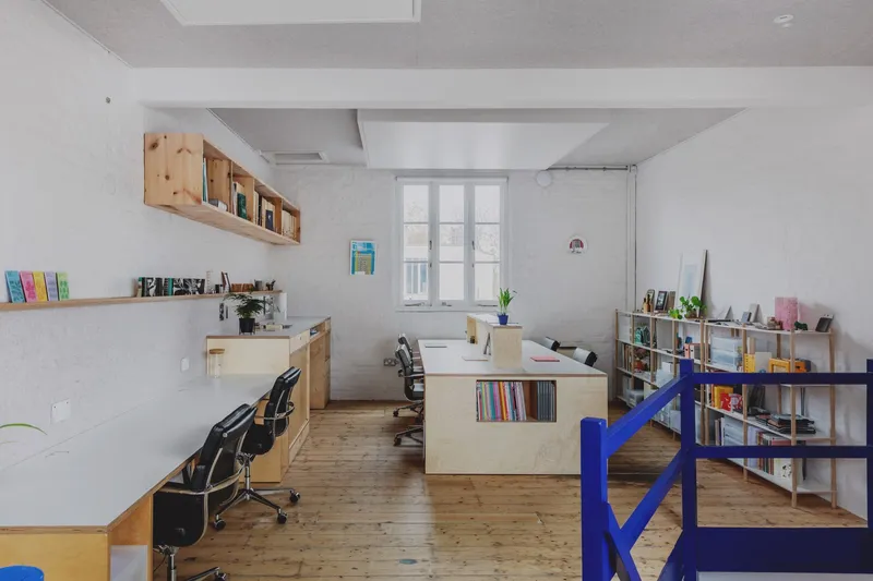 Work studio with plywood desks and blue metal railing overlooking the lower level