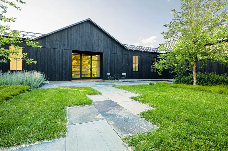 Garden view of the black timber-clad gable form with a stone paver path cutting through mown lawn