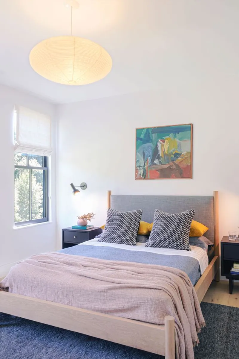 Bedroom with a paper globe pendant fixture, light wood bed frame and black-framed window overlooking greenery