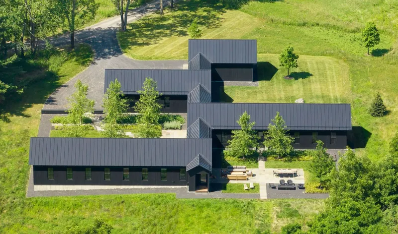 Aerial view of staggered dark timber-clad volumes with standing seam metal roofs arranged across a landscaped lawn