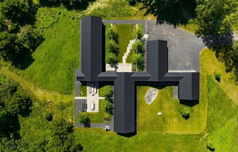 Drone view showing the pinwheel plan of four black-clad wings around a central courtyard with planted trees
