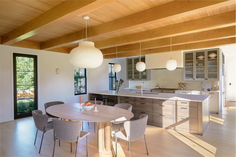 Open kitchen and dining area with exposed timber ceiling beams and pendant lights casting afternoon shadows