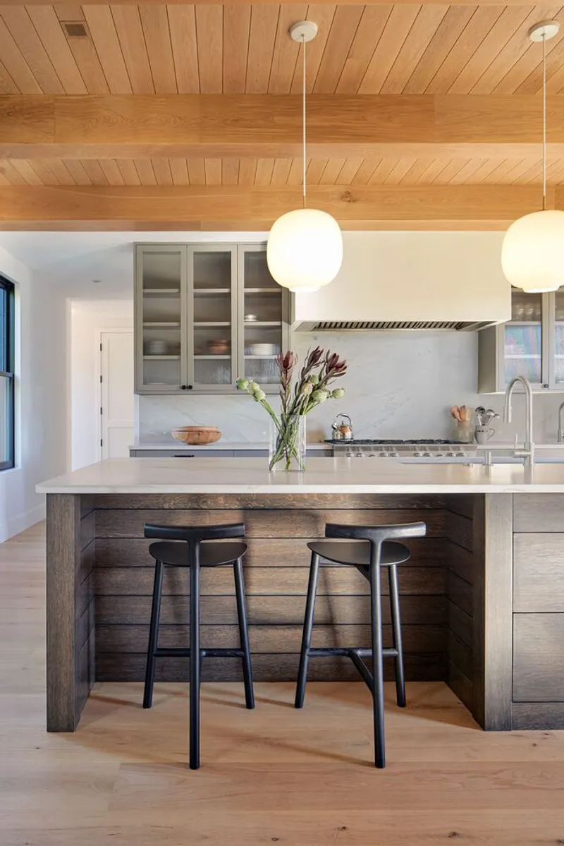 Kitchen island clad in dark horizontal timber boards with marble countertop and globe pendant lights overhead