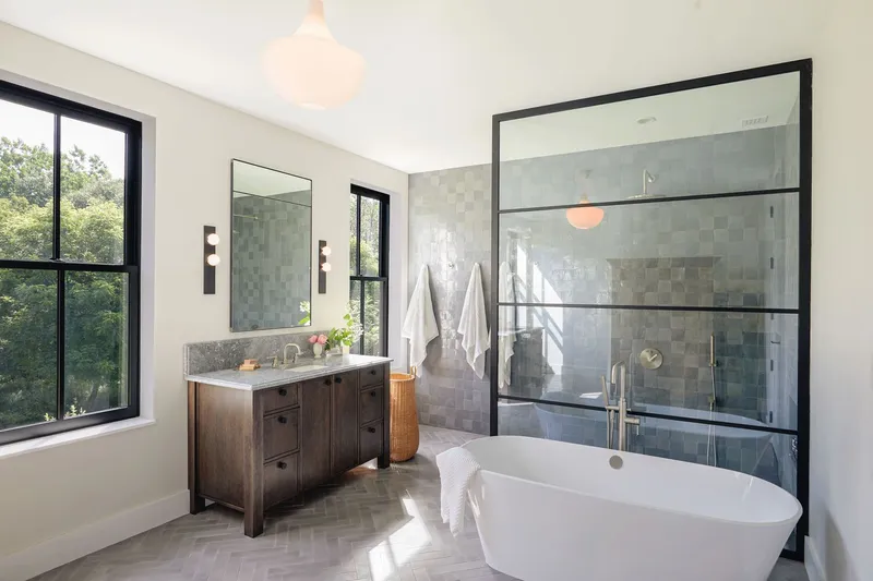 Bathroom interior with freestanding tub, black-framed glass shower enclosure and variegated grey tile backsplash in morning light