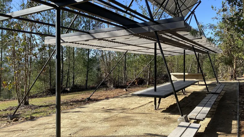Side view of the open-air pavilion with tensioned roof, benches, and surrounding woodland