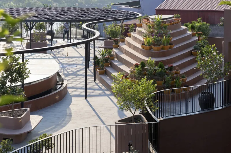 Rooftop terrace with tiered planters holding trees and shrubs framed by curved metal railings in bright daylight