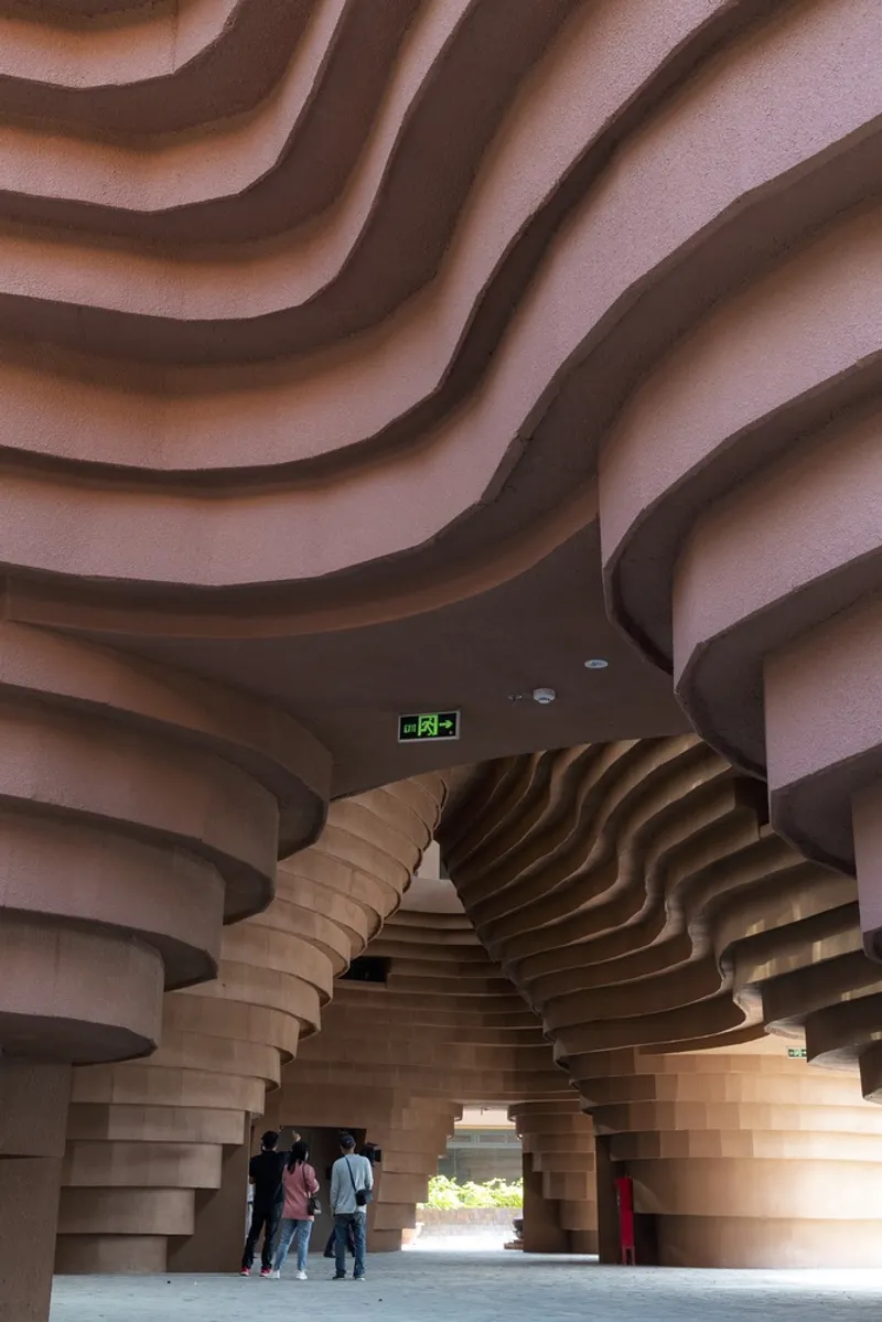 Undulating ribbed ceiling sweeping over sculptural columns as visitors gather near the sunlit exit